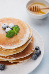A stack of delicious pancakes with honey and blueberries on a light blue background