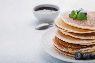 A stack of delicious pancakes with honey and blueberries on a light blue background. with copy space