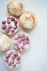 Delicious lemon and raspberry tartlets with meringue on a white vintage plate. Sweet treat on a light blue background. Flat lay and copy space. Top view