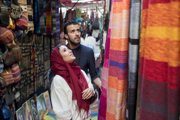 Obraz na płótnie Canvas Smiling young muslim couple shopping carpets in a textile store