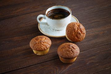 White cup of coffee and three cupcakes on dark wooden background
