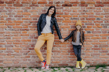 Motherhood, relationship and style concept. Fashionable young mother in leather jacket and sport...