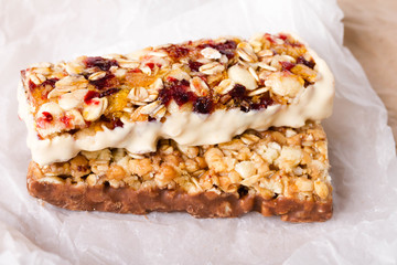 Energy bar on white paper. The cereal bar consists of oatmeal, honey, cranberries, raisins, nuts and dried apricots.