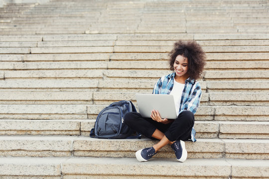Smiling student sitting on stairs using laptop
