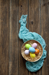 Multicolored eggs in a basket on a vintage wooden background. Easter concept, top view