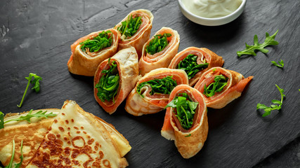 Crepes pancakes rolls with smoked salmon stuffed with wild rocket salad filling served on stone board with fresh creme