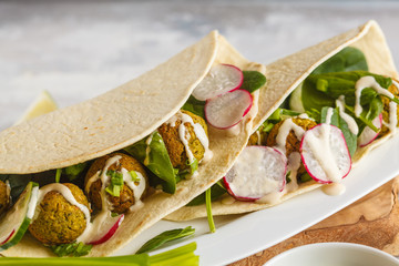 Vegan falafel with vegetables and tahini dressing in tortilla on a white dish. Vegan healthy food, Arabic food.