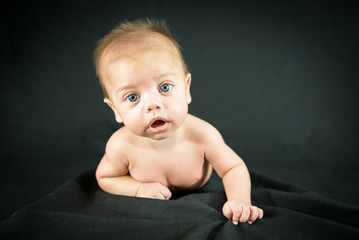 Blue eyed naked baby lying on black fabric
