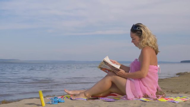 Beautiful woman in a silk beach shawl reads an interesting book. She is sitting and reading a book turning the pages. After she cleans the book and rests.