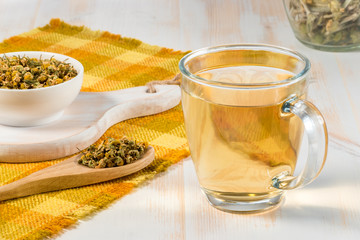 Cup of chamomile tea with dry chamomile flowers  on white wooden background.