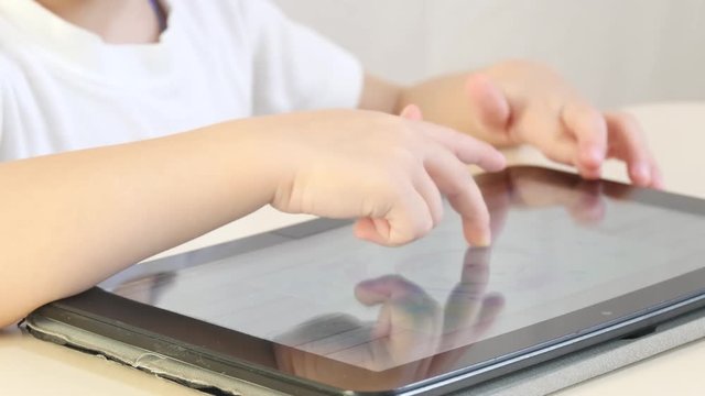 The child's fingers touch the electronic display of the tablet, press the virtual buttons. Close-up. The child is playing electronic games. The concept of child development.