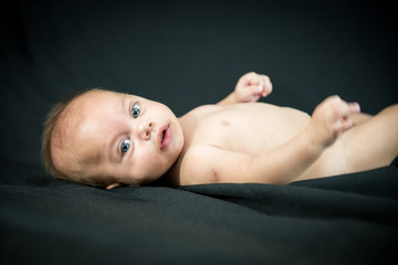 Blue eyed naked baby lying on black fabric