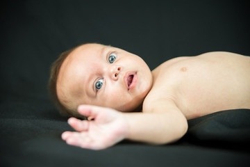 Blue eyed naked baby lying on black fabric