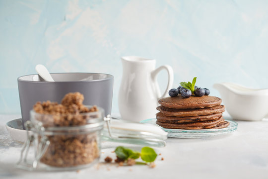 Chocolate pancakes, chocolate baked granola in a glass jar and milk. Healthy breakfast concept.