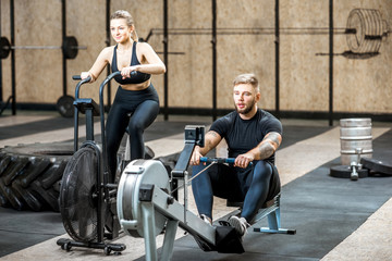 Fototapeta na wymiar Young couple training on the exercise air bicycle and rowing machine in the gym