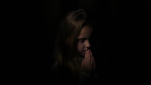 Beautiful face of earnestly praying little girl at night. 