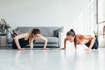 Fototapeta na wymiar Two fitness women warming up doing push-ups exercise working out at home