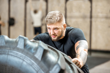 Obraz na płótnie Canvas Athletic man in black sportswear pushing a big tire training in the gym
