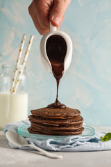Chocolate pancakes with chocolate syrup, chef pours liquid chocolate from a sauce-boat. Blue background, breakfast concept, cooking food.