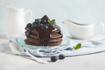 Chocolate pancakes with chocolate syrup, milk and blueberries. Blue background, breakfast concept, copy space