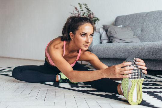 Fit woman doing stretching while sitting on the floor at home