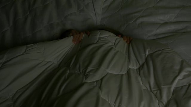 Scared girl hiding under blanket