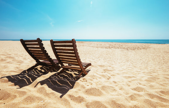 Two beach chairs on empty ocean beach under bright shining sun