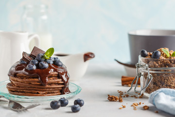 Chocolate pancakes with syrup and berries, chocolate granola and milk. Breakfast concept, blue background
