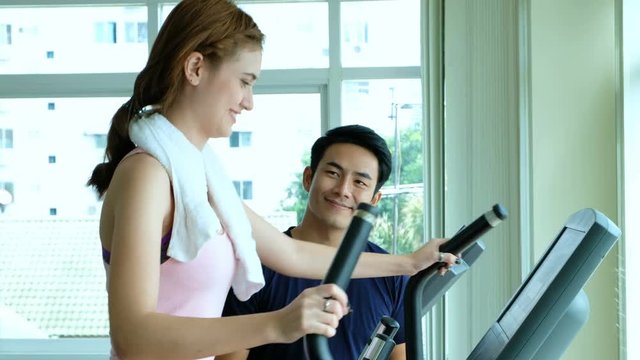 caucasian beautiful woman workout on treademill with asian man trainer in gym fitness center