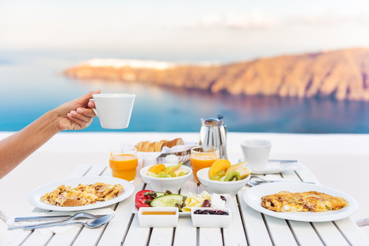 Breakfast woman drinking coffee at luxury hotel resort restaurant table Mediterranean sea view in Santorini, Oia, Greece. Female hand holding coffee cup at morning brunch. Eggs, fruit salad plate.