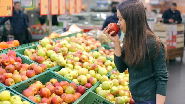 Woman selecting fresh red apples in grocery store produce department