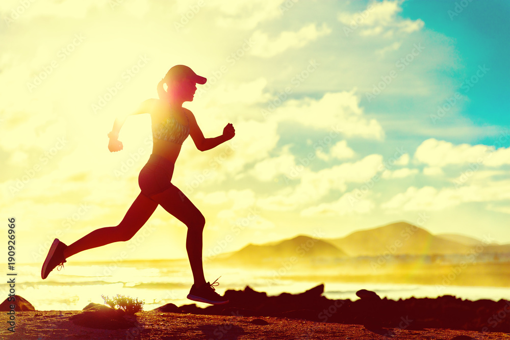 Wall mural summer fitness healthy active woman running on beach against sun flare at sunset. runner athlete spo