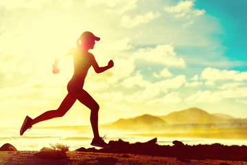 Summer fitness healthy active woman running on beach against sun flare at sunset. Runner athlete sport girl jogging on trail run race on nature landscape. Fit active lifestyle.