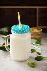 Mug Mason jar with a refreshing milkshake green spinach and pine nuts on a stone or slate background. Healthy vegetarian food. Stone background, copy space.