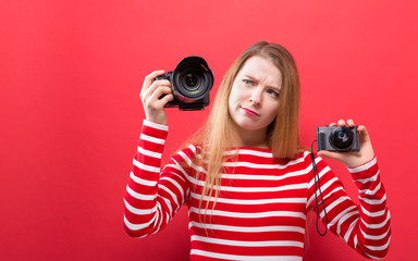 Young woman comparing professional and compact cameras on a solid background