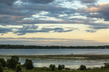 An expansive view of dark sunset clouds over Rock Lake in Wisconsin, USA give a moody feel to the large lake and marsh plants near the shore.
