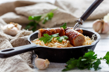 Frying pan with stewed sauerkraut and fried sausages.