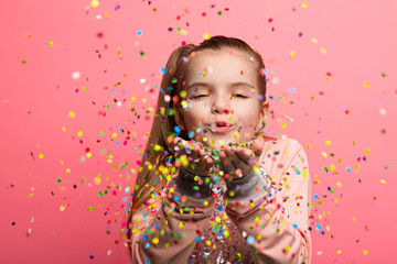 Obraz na płótnie Canvas Happy girl celebrating on a pink background. Blows up multicolored confetti