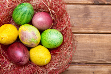 Colorful easter eggs in nest  on wooden background. Eggs handmade new style of colouring . Pattern, easter concept.