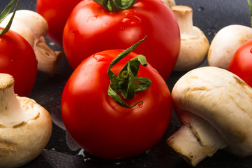 fresh tomatoes and mushrooms - champignons on black plate