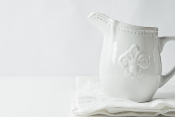 White Vintage Ceramic Cream Milk Jug Standing on Folded White Cotton Linen Napkin on Table. Holiday Baking Workshop Poster. Nordic Kitchen Interior. Styled Image for Social Media Blog