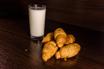 Plate with fresh croissants and glass of milk on a dark wooden table