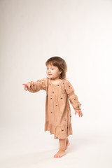 Cute little girl in beige dress isolated on white background. Portrait of happy little girl on white background. Sweet girl with curly hair.