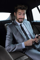 man in suit sitting in car and reading messages on smartphone