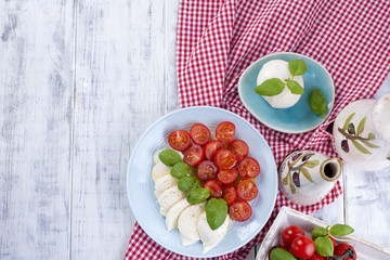 Italian salad with caprese. Salad of fresh vegetables and cheese. Ceramic tableware. Free space for text. Towel in a red cage.