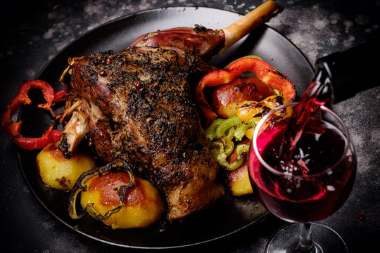 Roasted lamb shank with spices and grilled vegetables and red wine glass poured with wine