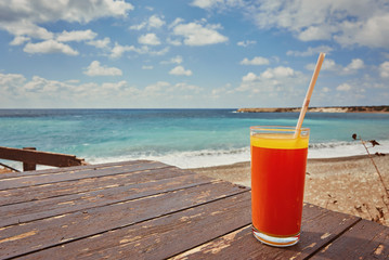 Melon juice on a sea beach. Glasses with red drink and straw stands on a fallen coconut.