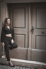 Beautiful woman in stylish black clothes - Young confident woman, in an elegant, modern black outfit, leaned against a wall, in front of a big vintage wooden door, looking up.