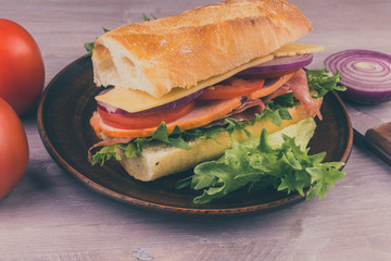 Fresh sandwich of baguette with ham, cheese, lettuce, onions and tomatoes