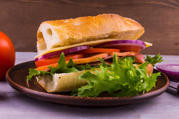 Fresh sandwich of baguette with ham, cheese, lettuce, onions and tomatoes